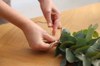 Çiçekçinin ahşap masasında okaliptüs dallarından güzel bir buket yapıyor.