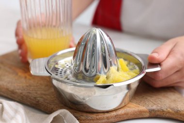 İçerideki masada taze sıkılmış portakal suyu ve meyve sıkacağı olan kadın, yakın plan.