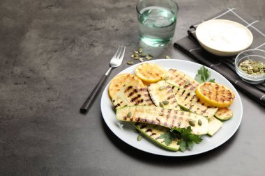 Lezzetli ızgara kabak dilimleri, balkabağı çekirdekleri, limon ve maydanoz gri desenli masa, yakın plan.
