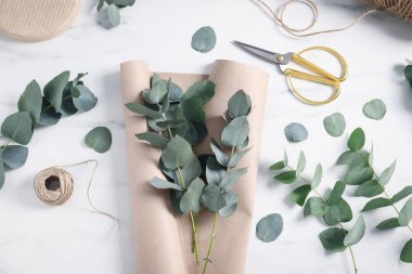 Çiçekçi. Okaliptüs dalları, iplik, makas ve ambalaj kağıdı beyaz mermer masa, düz yatıyordu