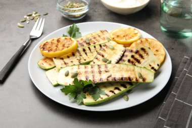 Lezzetli ızgara kabak dilimleri, balkabağı tohumları, limon ve maydanoz gri masada, yakın plan.