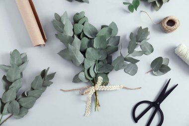 Çiçekçi. Okaliptüs dalları, iplikler, ambalaj kâğıdı ve makas beyaz masada, düz yatıyordu.