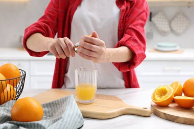 Meyve suyu. İçerideki beyaz mermer masada portakal suyu kullanan kadın, yakın plan.