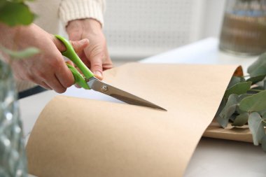 Çiçekçi, çiçekçide beyaz masada okaliptüs dallarından güzel bir buket yapıyor.