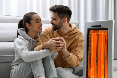 Bir çift evde elektrikli ısıtıcının yanında ellerini ısıtıyor.