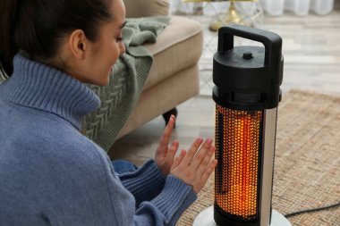 Evdeki elektrikli ısıtıcının yanında ellerini ısıtan kadın.