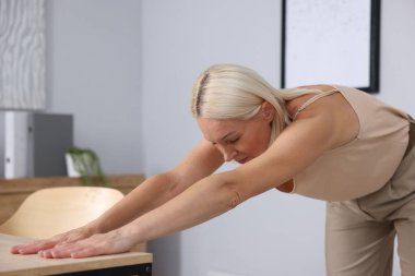 Olgun bir kadın ofiste masaya yaslanıyor.