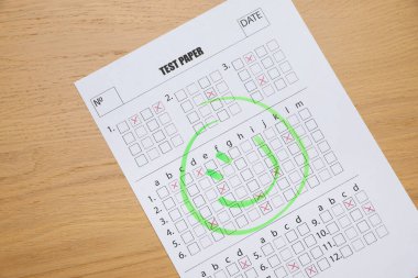 Tahta masaya çizilmiş gülen yüzlü cevap kağıdı, üst manzara. Öğrenci sınavını geçti