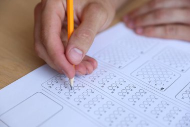 Tahta masada çoklu seçim testi dolduran öğrenci, yakın çekim. Sınavı geçmek