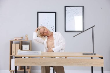 Gri duvarın yanındaki masada uzanan olgun bir kadın.