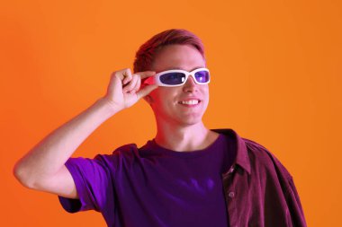 Turuncu arka planda güneş gözlüğü takan gülümseyen adam.