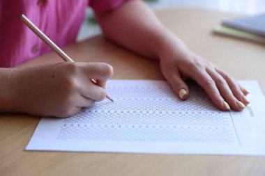 Tahta masada çoklu seçim testi dolduran öğrenci, yakın çekim. Sınavı geçmek