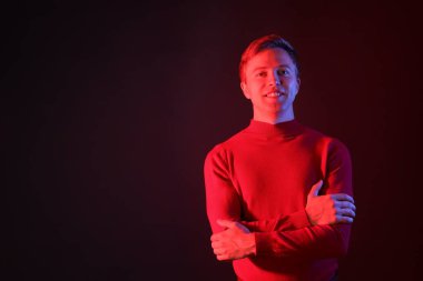 Koyu arkaplana karşı neon ışıklarda çapraz kollu gülümseyen adamın portresi. Metin için boşluk