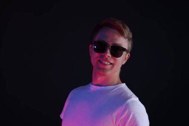 Siyah arka planda, neon ışıklarda güneş gözlüğü takan gülümseyen adam