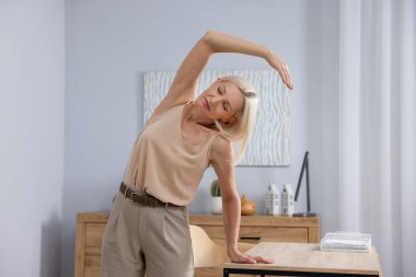 Olgun bir kadın ofiste masaya yaslanıyor.