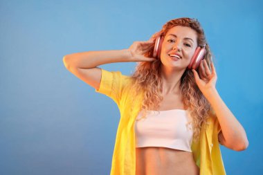 Kulaklıkla müzik dinleyen ve açık mavi arka planda dans eden mutlu kadın. Metin için boşluk