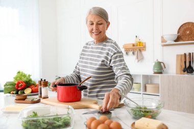 Üst düzey kadın mutfaktaki beyaz mermer masada yemek pişiriyor.