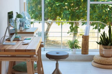 Ev çalışma alanı. Modern bilgisayar ve kırtasiye malzemeleri pencerenin yanındaki ahşap masada.