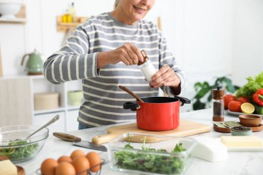 Üst düzey kadın mutfaktaki beyaz mermer masada yemek pişiriyor.