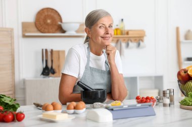 Üst düzey kadın mutfaktaki beyaz mermer masada yemek pişiriyor.