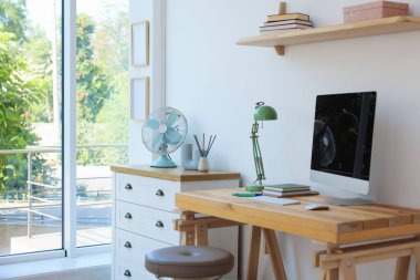 Ev çalışma alanı. Modern bilgisayar ve kırtasiye malzemeleri pencerenin yanındaki ahşap masada.