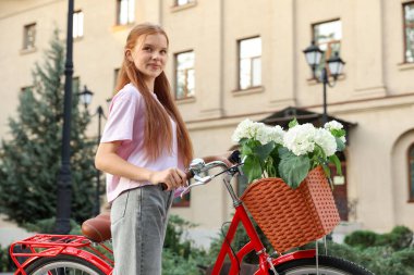 Bisikletin yanında güzel bir genç kız, şehir caddesinde bir sepet çiçekle, alçak açılı bir manzara.
