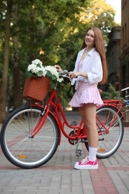 Bisikletin yanında güzel bir genç kız ve şehir caddesinde bir sepet çiçek.