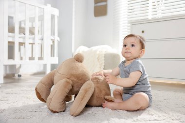 Küçük şirin bebek odada oyuncak ayıyla oynuyor.