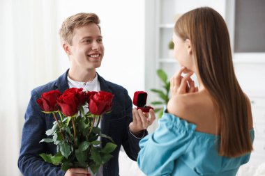 Nişan yüzüğüyle ve gül buketiyle gülümseyen bir adam kız arkadaşına evlenme teklif ediyor.