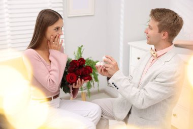 Nişan yüzüğü ve gül buketi olan bir adam evde duygusal kız arkadaşına evlenme teklif ediyor. Bokeh etkisi