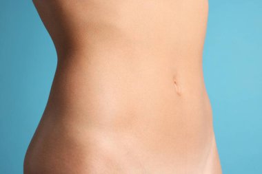 Açık mavi arka planda düz göbekli kadın, yakın plan.