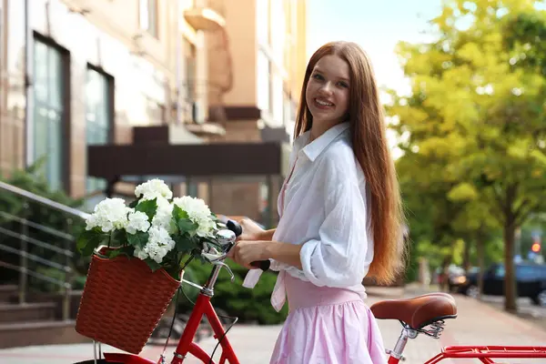 Bisikletin yanında güzel bir genç kız ve şehir caddesinde bir sepet çiçek.