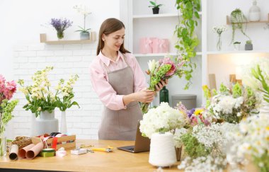 Profesyonel çiçekçi dükkandaki ahşap masada çiçek buketi yapıyor.