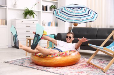 Güneş gözlüklü mutlu adam ve şişme yüzüklü paletler evde yerde eğleniyor. Denizde tatilin hayalini kuruyorum.