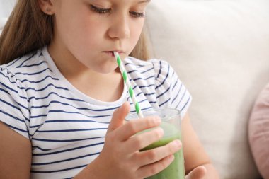 Küçük kız evdeki kanepede samandan meyve suyu içiyor.