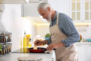 Mutfaktaki mutfağın tepesinde yaşlı bir adam yemek pişiriyor.
