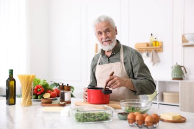 Mutfaktaki beyaz mermer masada yaşlı bir adam yemek pişiriyor.
