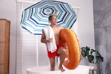 Şişme yüzüklü, dalış maskeli, havlulu ve kumsaldaki şemsiyeli mutlu adam küvette. Denizde tatilin hayalini kuruyorum.