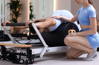 Stüdyoda pilates eğitmeni tarafından yönetilen reformcu kadın üzerinde egzersiz yapıyor.