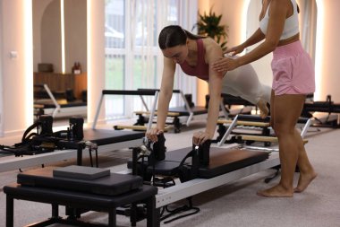 Stüdyoda pilates eğitmeni tarafından yönetilen reformcu kadın üzerinde egzersiz yapıyor.