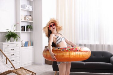 Güneş gözlüklü, hasır şapkalı, şişme yüzüklü mutlu kadın evde eğleniyor. Denizde tatilin hayalini kuruyorum.