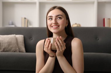 Evdeki kanepenin yanında bir bardak içkiyle güzel bir kadın.