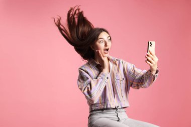 Pembe arka planda akıllı telefon kullanan ceketli, güzel, uzun saçlı bir kadın. Metin için boşluk