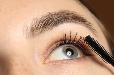 Kahverengi arka planda kirpiklerine rimel süren kadın, yakın plan.