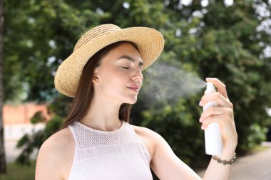 Hasır şapkalı gülümseyen kadın yüzüne termal su püskürtüyor.