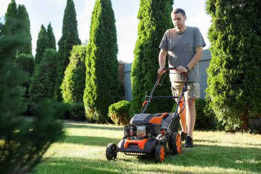Bahçede çim biçme makinesiyle yeşil çim biçen bir adam