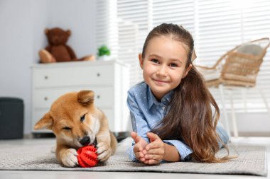 Evinde yerde köpeği ve evcil oyuncağıyla küçük şirin bir kızın portresi.