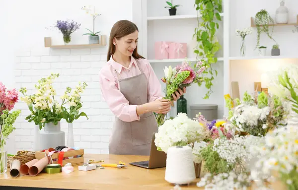 Profesyonel çiçekçi dükkandaki ahşap masada çiçek buketi yapıyor.