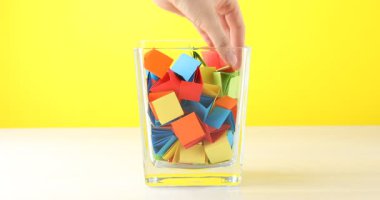 Ahşap masadaki cam kavanozdan turuncu kağıt parçası alan kadın, yakın plan.