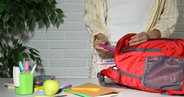 Masada kırmızı sırt çantasından defterleri alan kadın, yakın plan.